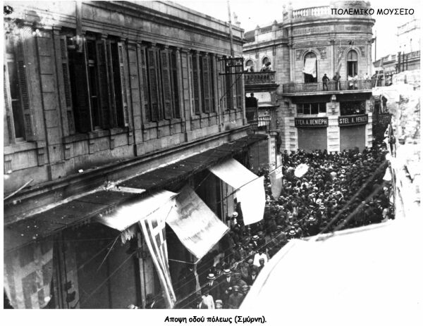 View of a crowded street, with Hellenic flags on the foreground.